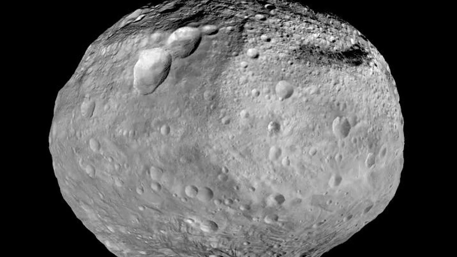 L'astéroïde Vesta photographié par la sonde Dawn, montrant une surface criblée de cratères, une immense dépression à son pôle sud et de longues rainures équatoriales.