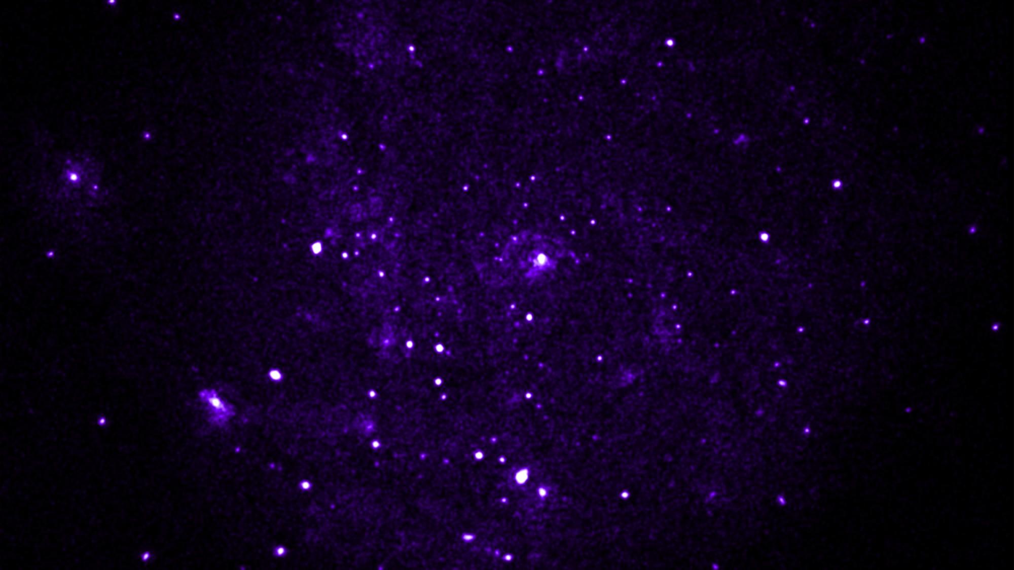 La galaxia del Molinete vista solo en rayos X blandos, con puntos luminosos dispersos sobre un fondo morado difuso.