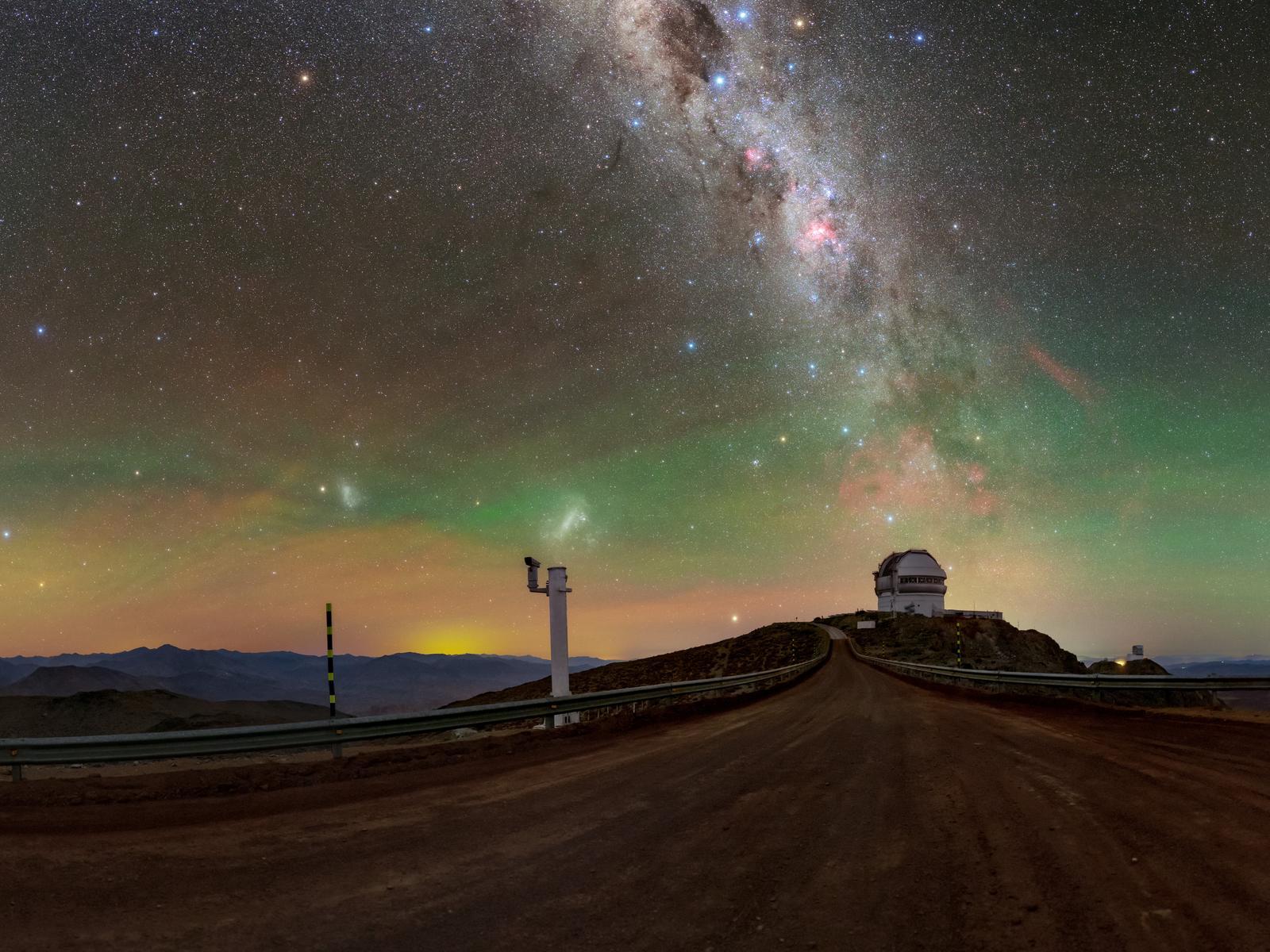 El cielo estrellado sobre el observatorio de Cerro Pachón, en Chile, con la Vía Láctea y, junto al horizonte, un resplandor amarillo anaranjado procedente de una ciudad cercana.