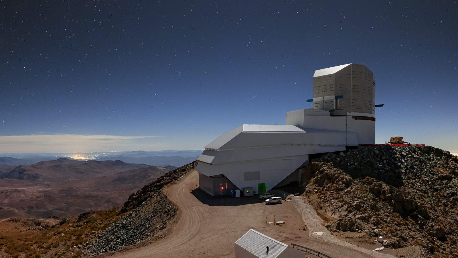 Vista nocturna del cielo sobre el observatorio Vera C. Rubin, con un cielo azul profundo, estrellas visibles y grupos de luces artificiales en el horizonte.