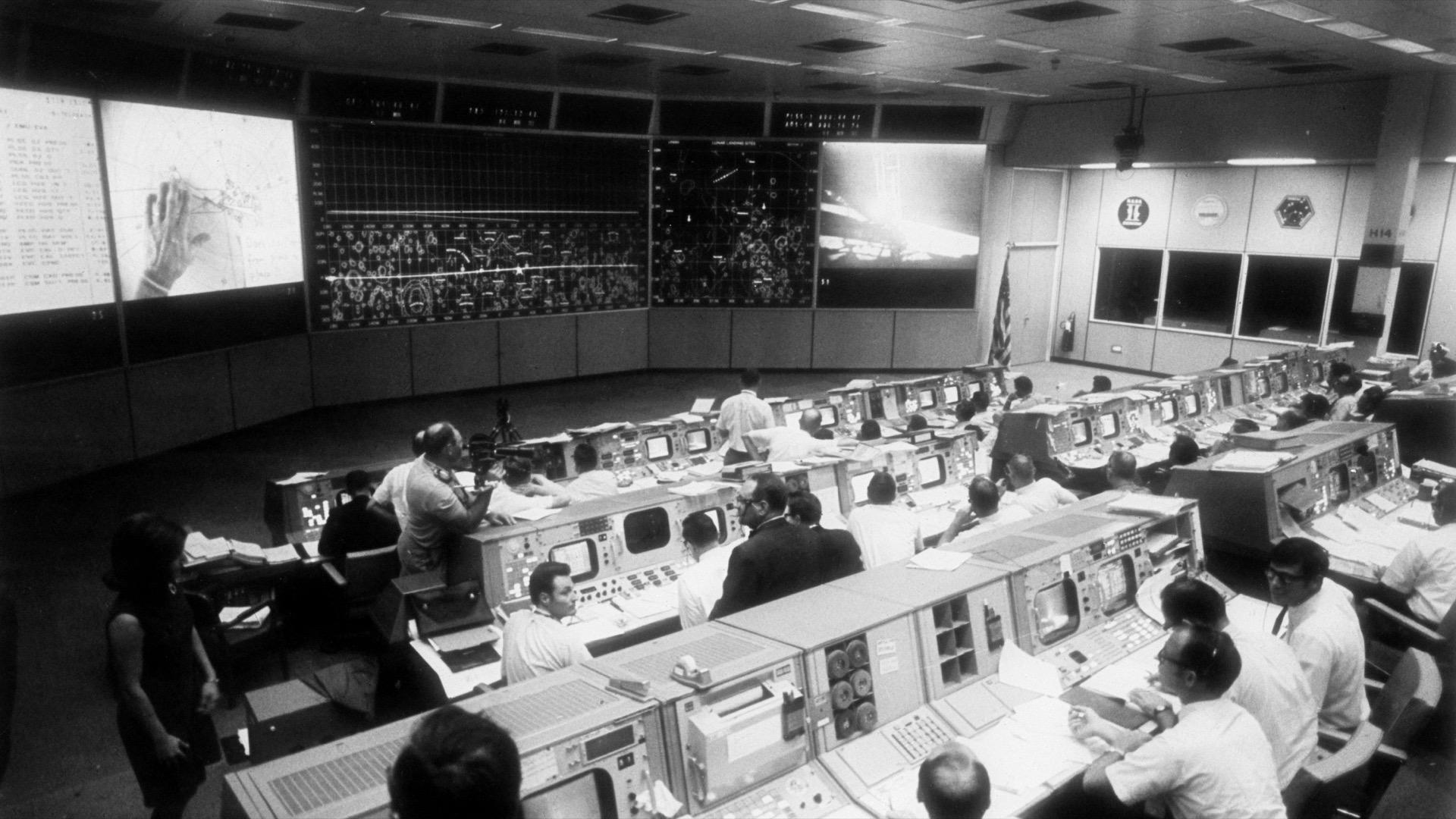 Vue de la salle de contrôle de la mission Apollo 11, remplie de consoles et d'écrans, quelques instants après l'alunissage.