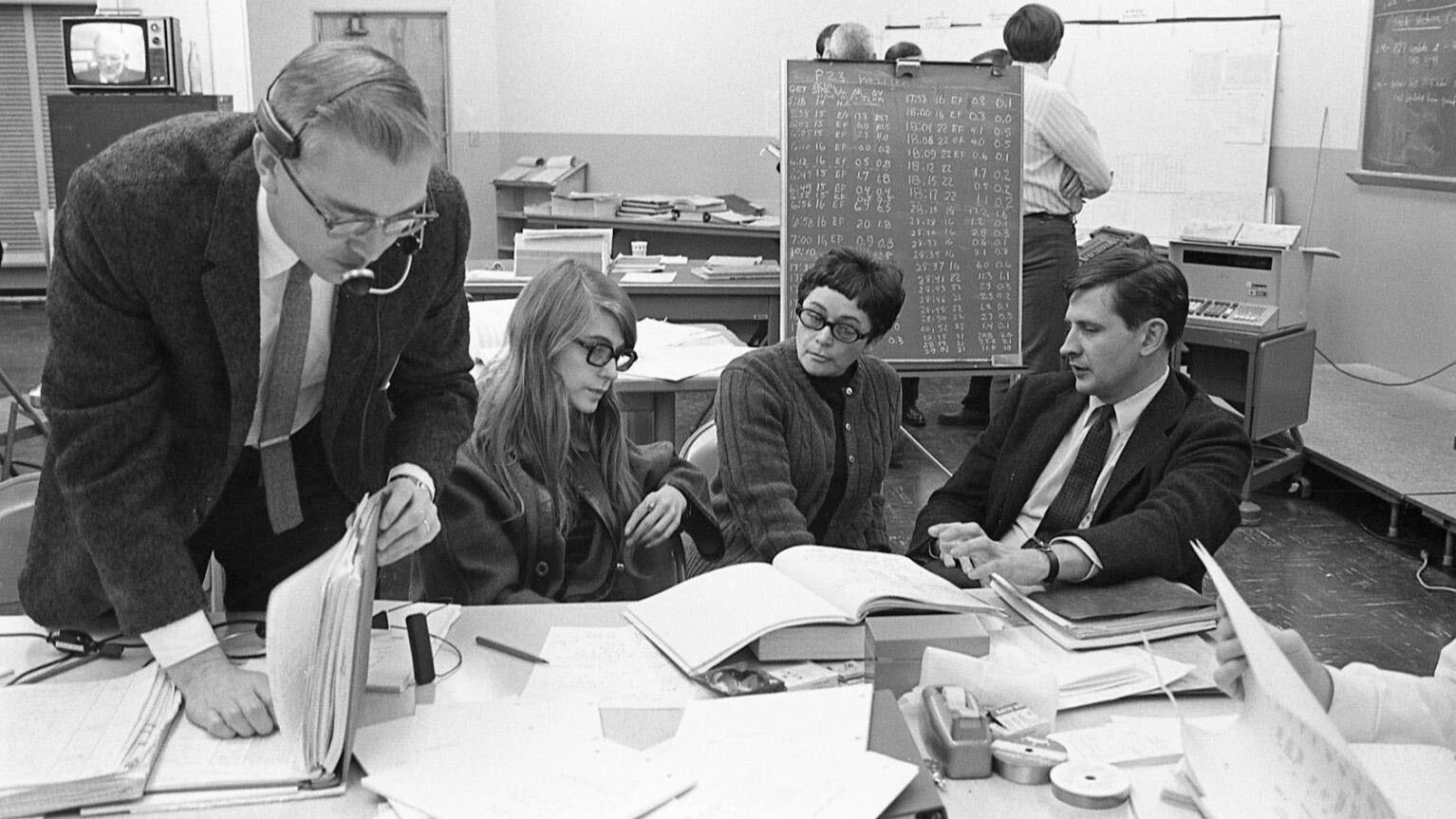 Quatre ingénieurs du MIT travaillent ensemble devant un tableau noir couvert d'un programme de navigation pour le module de commande lunaire.