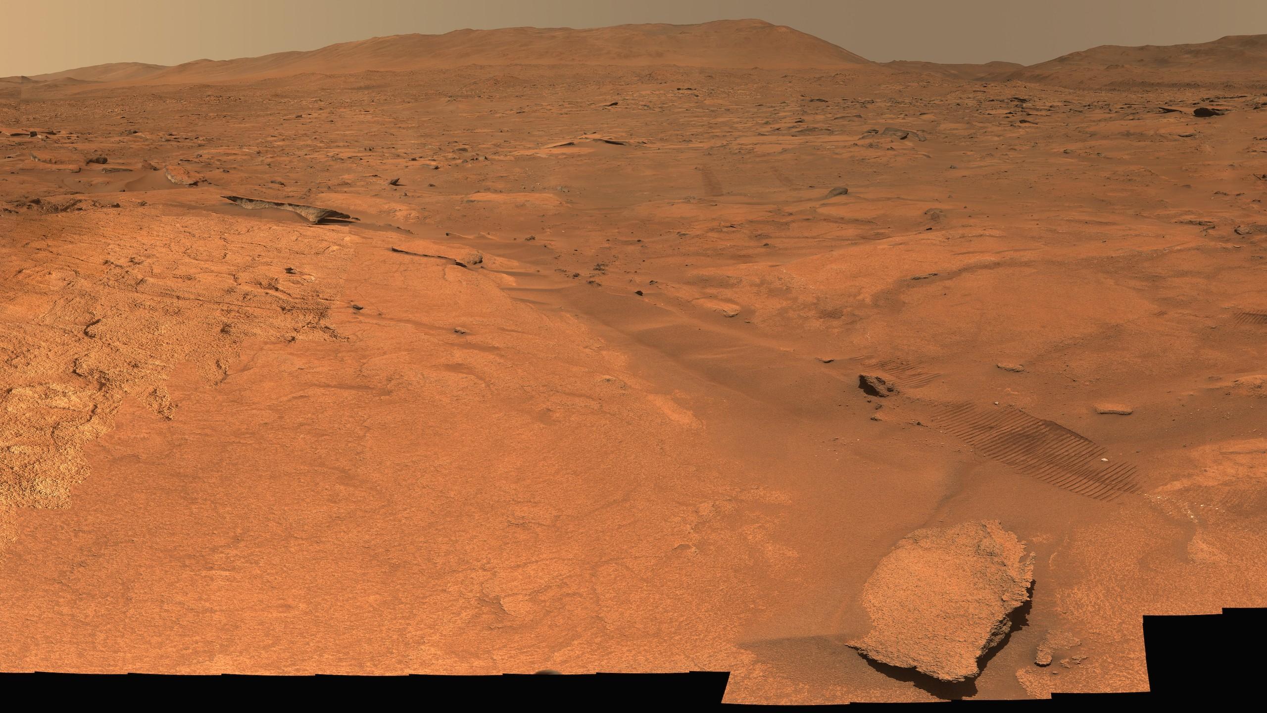 Natural-color Mastcam-Z panorama of the Margin Unit at Jezero crater: rust-colored rocky ground, a strip of pale bedrock, and the dark silhouettes of the rover in the foreground.