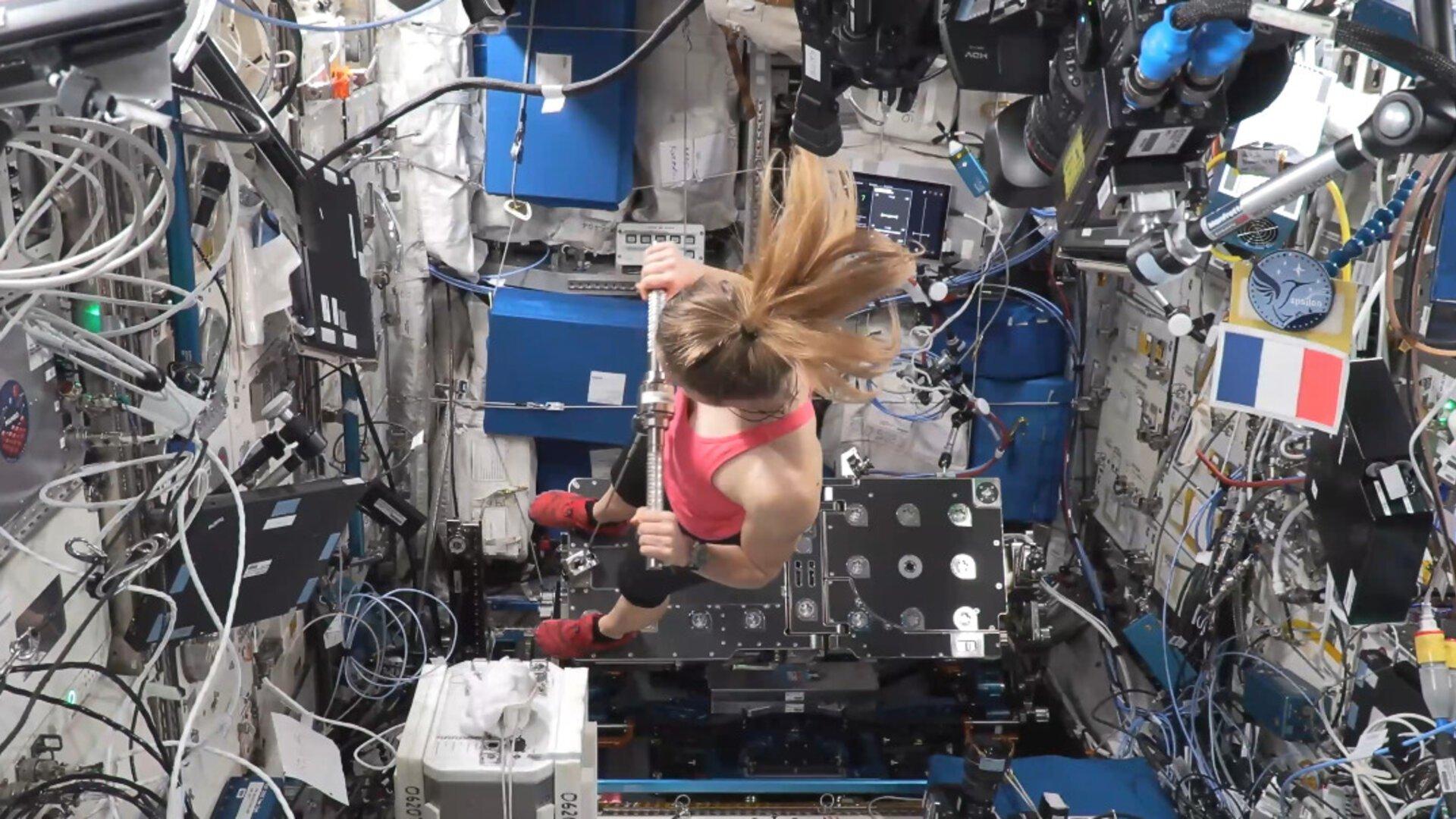 Sophie Adenot, in workout clothes, tests the new European E4D exercise device inside the Columbus module, in a rowing position secured to the floor by straps.