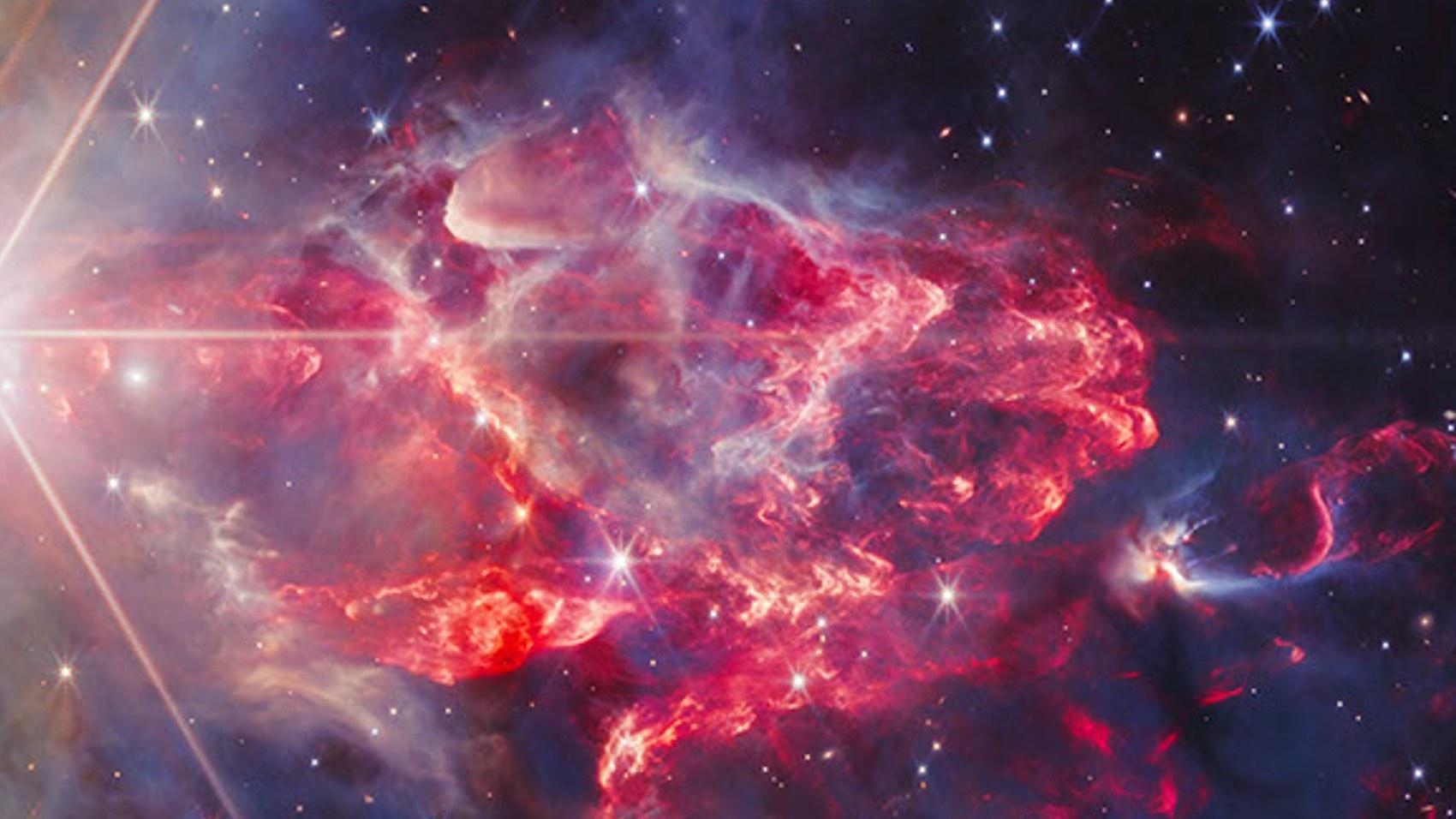 Close-up of the reddish region of NGC 7129: a plume of red and gray dust from which protostars emerge, punctuated by jets of ejected material.