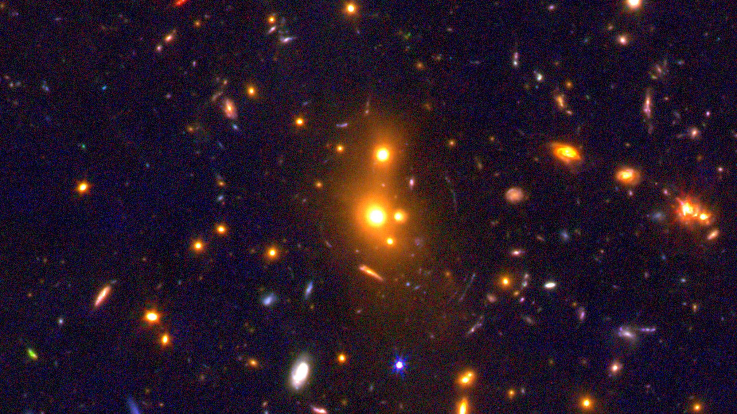 Imagen compuesta del telescopio James Webb que muestra el cúmulo de galaxias XLSSC 122: un grupo de manchas anaranjadas en el centro, rodeado de arcos azulados de galaxias lejanas deformadas por la gravedad del cúmulo.
