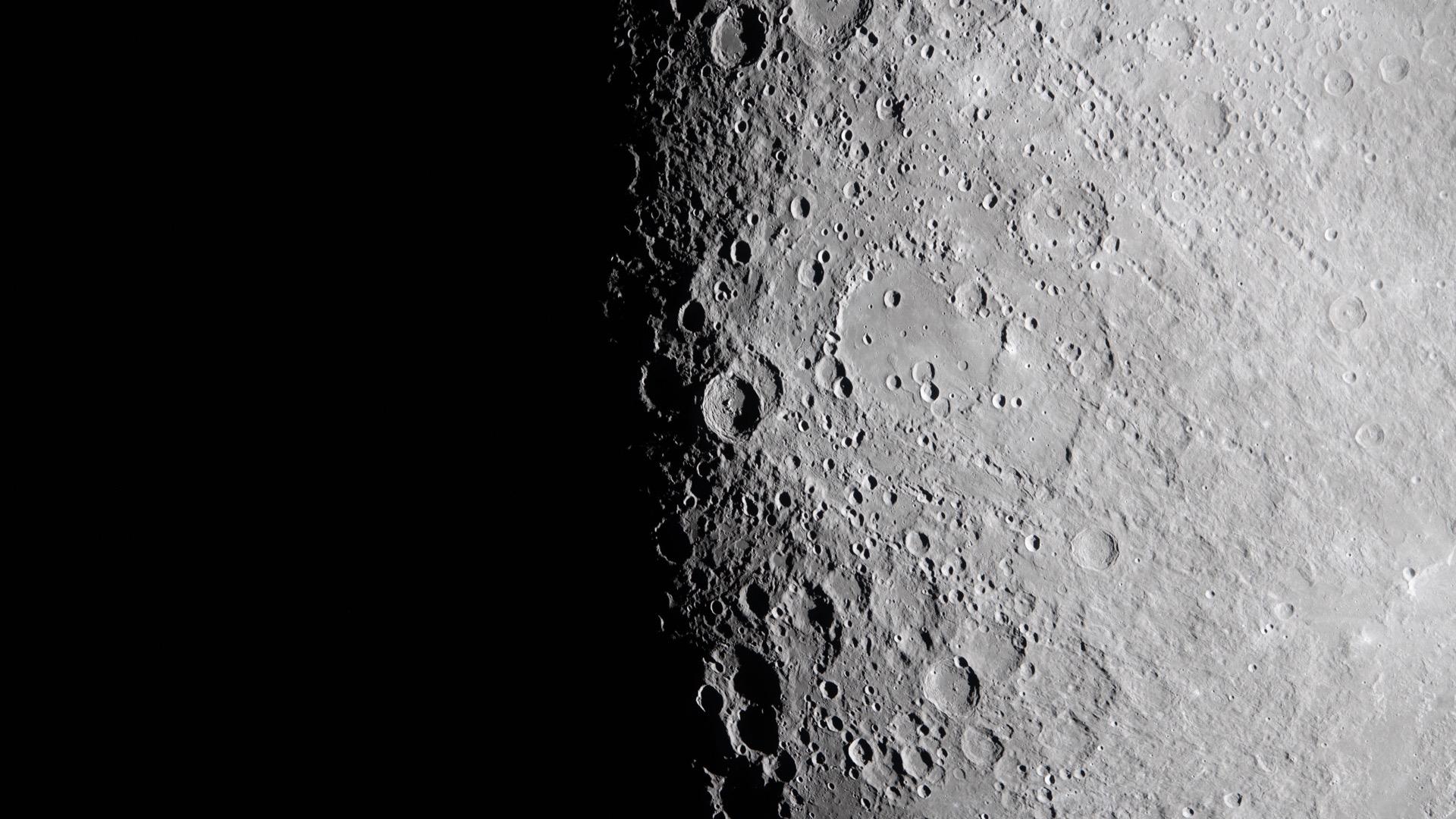 The lunar surface seen from the Orion capsule at the boundary between day and night: a heavily cratered grey terrain lit at a grazing angle, while the left half falls into darkness.