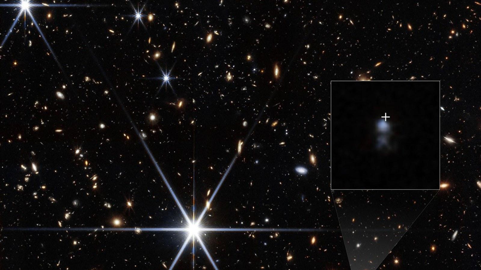 A field of distant galaxies seen by Webb, with two fuzzy blue smudges at the center and a small galaxy boxed in white on the right, marking where the radio burst came from.