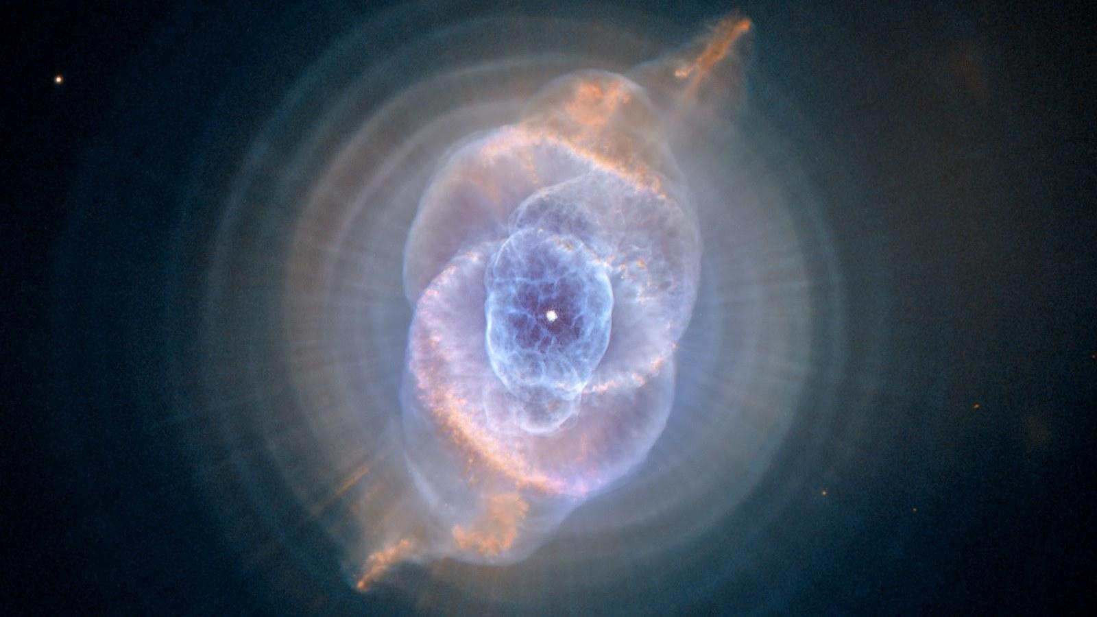 Imagen de Hubble de la nebulosa Ojo de Gato: una nube de gas azul y naranja con formas concéntricas y una estrella central brillante.