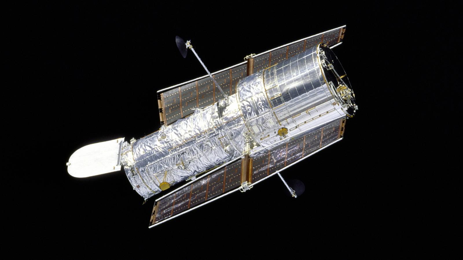 Le télescope spatial Hubble photographié en orbite par l'équipage de la navette Discovery, ses panneaux solaires et son manteau thermique doré bien visibles, la porte d'ouverture de 3 mètres grande ouverte.