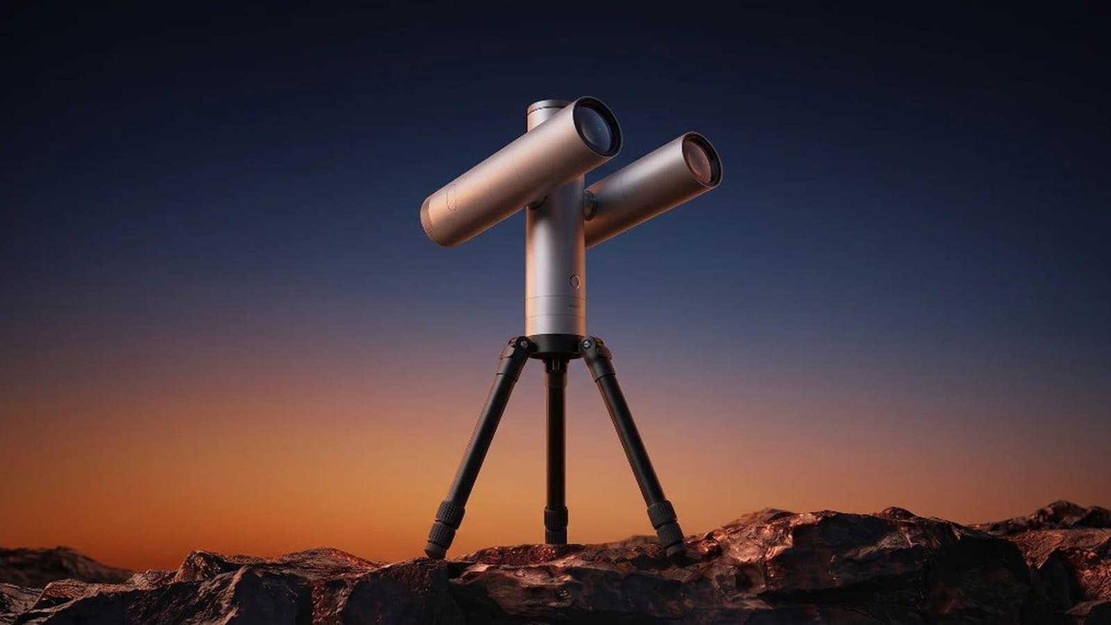 El telescopio Atlas de Vaonis en su conjunto, con sus dos módulos de imagen de 80 mm montados sobre la montura y el trípode, posado en un suelo rocoso bajo un cielo crepuscular azul y anaranjado.