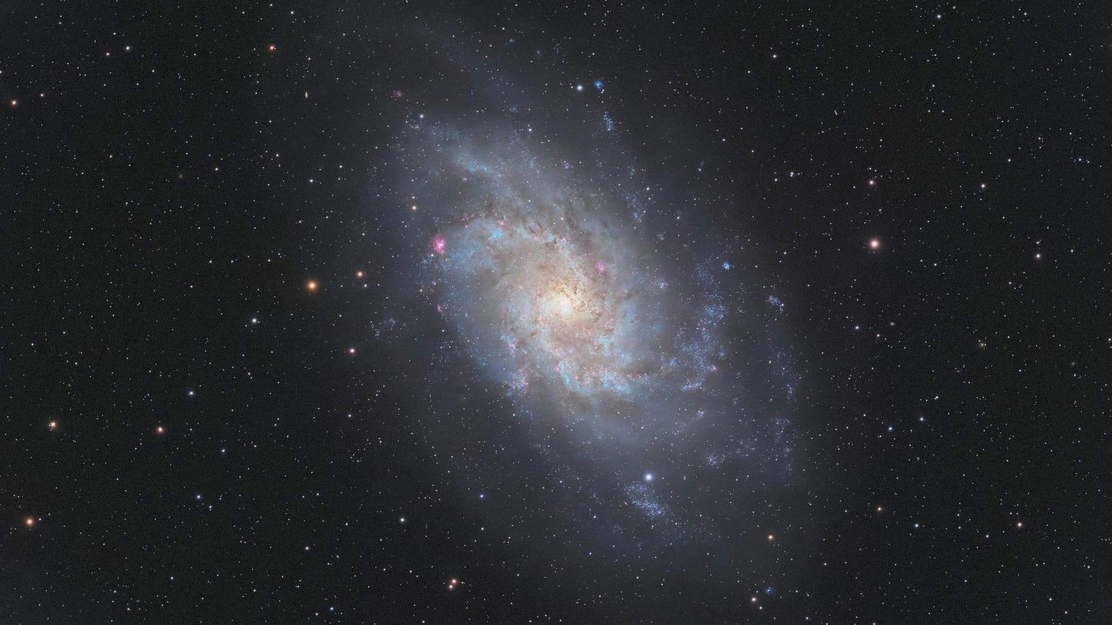 La galaxia del Triángulo fotografiada por Atlas: una espiral azulada vista de frente, rodeada de nubes de estrellas más frías.