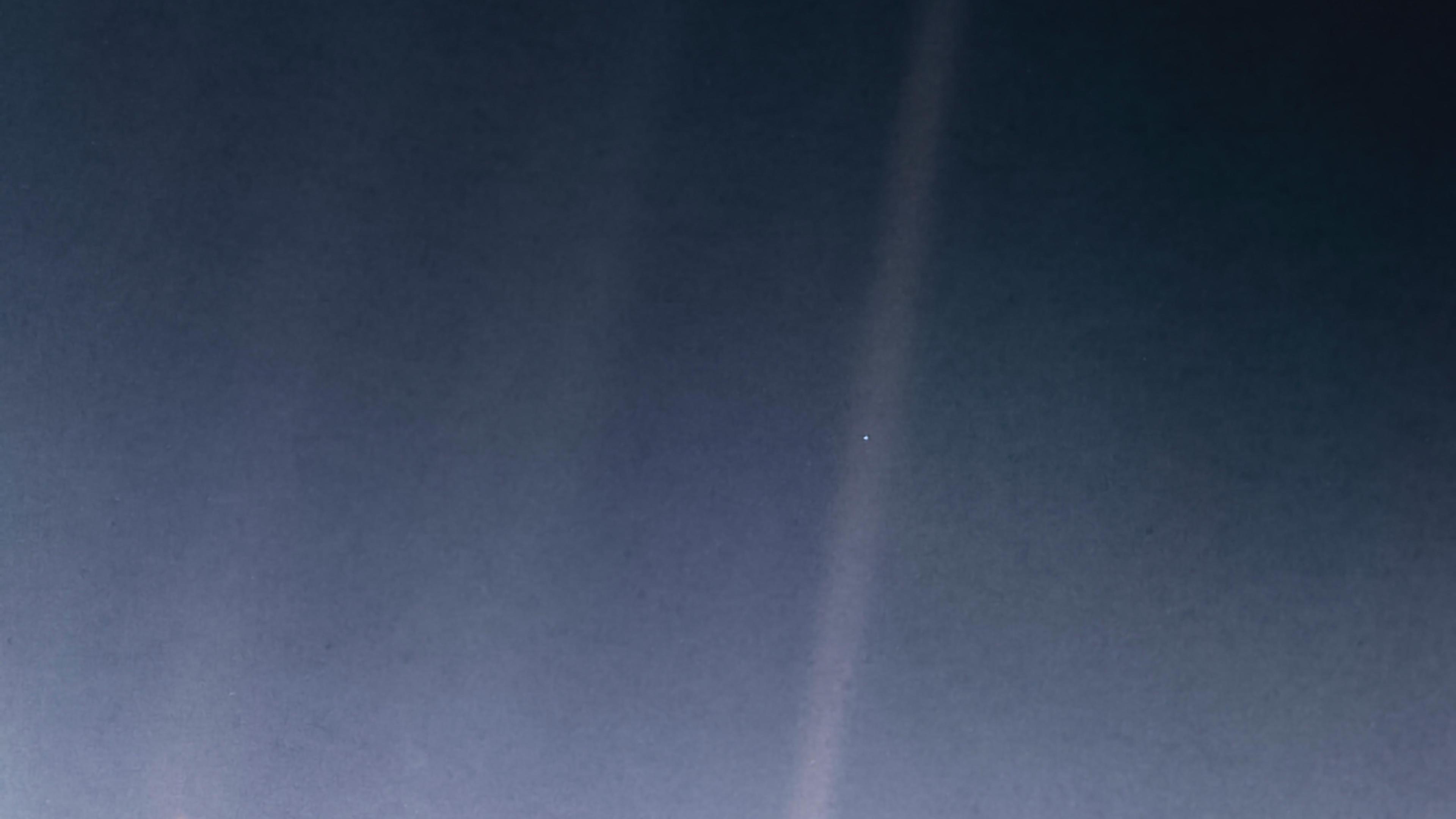 Image retravaillée par la NASA en 2020 : un étroit rayon de lumière diagonal traverse un fond noir, avec un unique point bleu pâle en son centre, la Terre photographiée depuis 6 milliards de kilomètres.