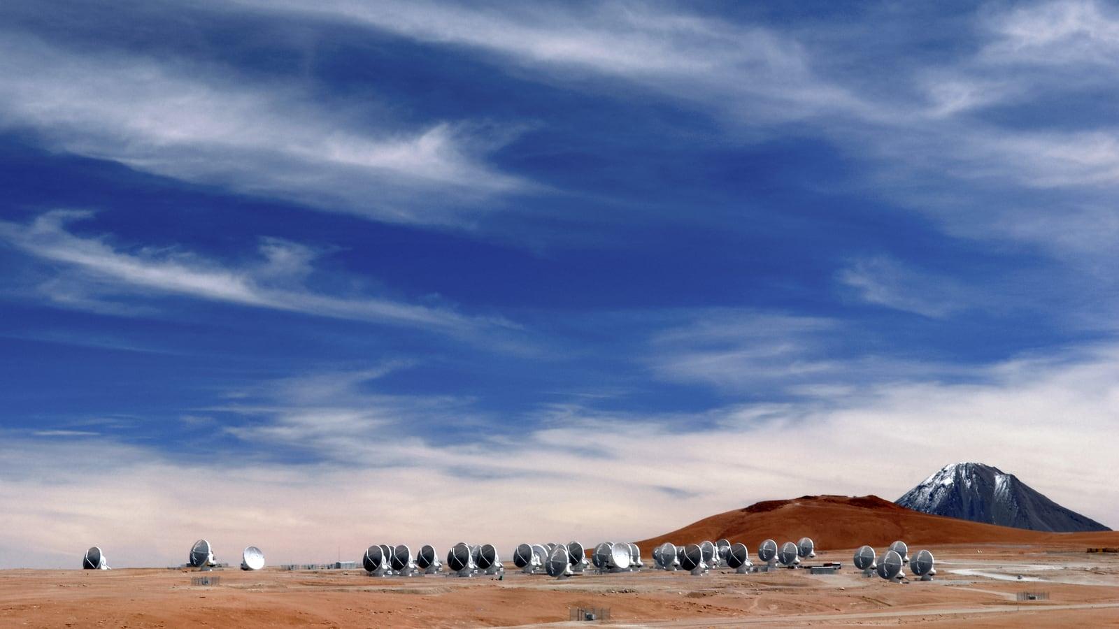 Panoramic view of the Chajnantor plateau in the Atacama desert, with the dish antennas of the ALMA radio telescope lined up under a clear sky.