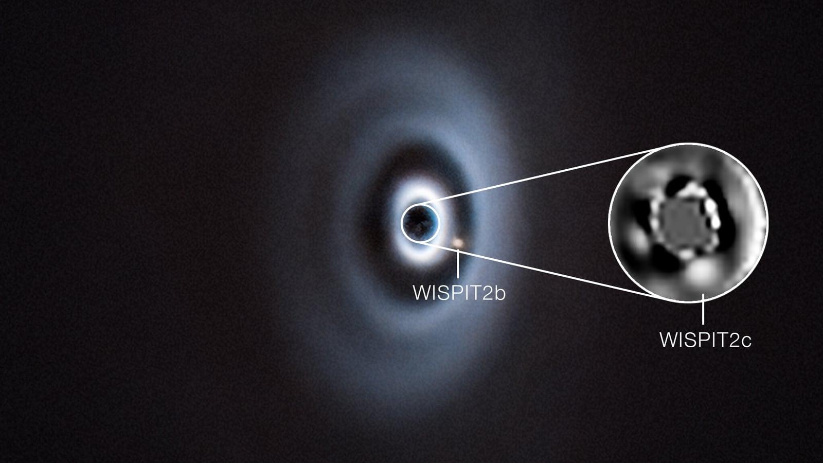 Image of the WISPIT 2 disk taken with the SPHERE instrument on the VLT: a tilted disk crossed by bright concentric rings and dark gaps, with one bright dot inside a gap and a second, closer to the star, shown in a magnified inset.