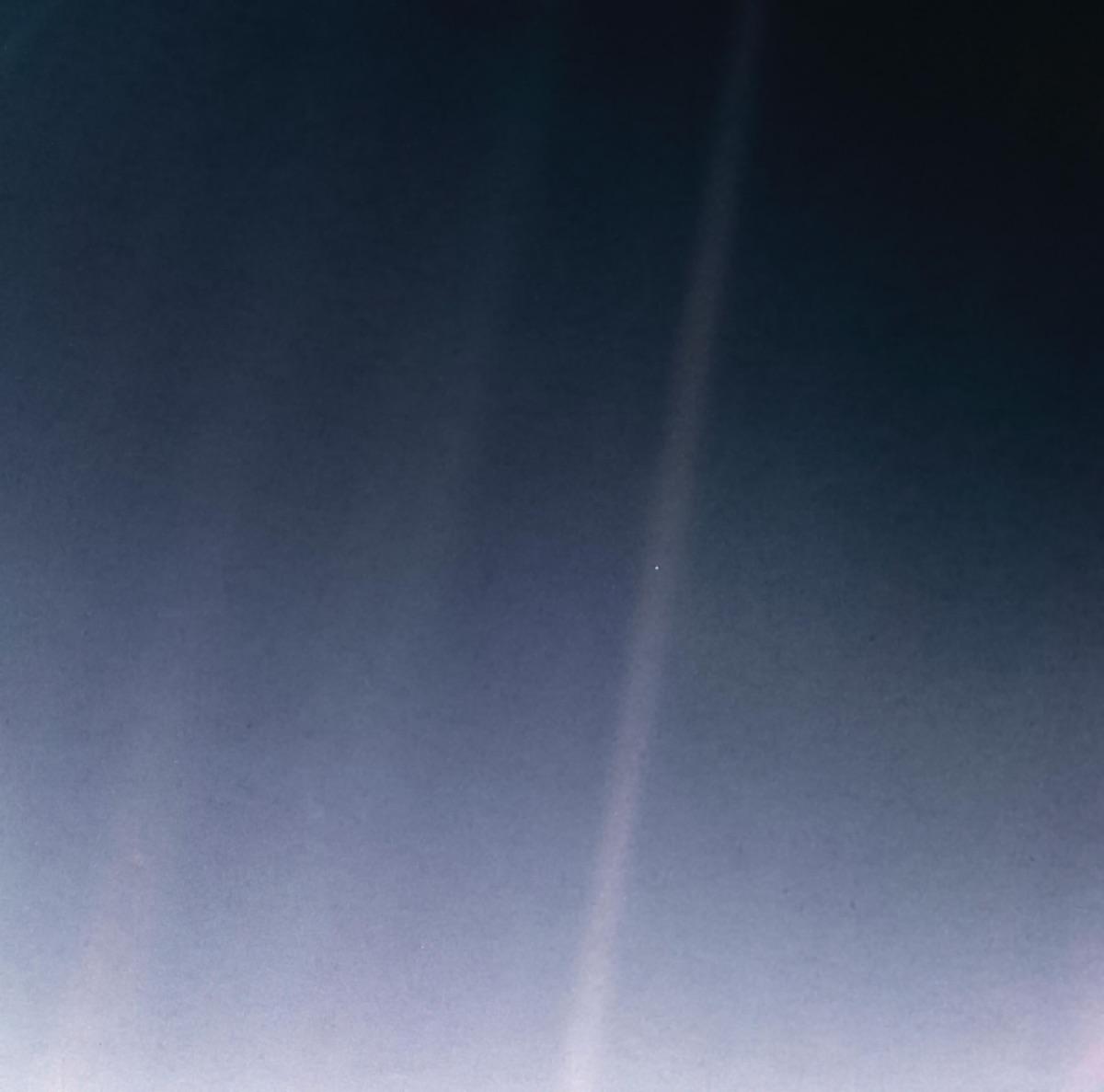 Earth photographed by Voyager 1 from 6 billion km away: a pale blue dot suspended in a sunbeam (the beam is visible at the top right of the image).